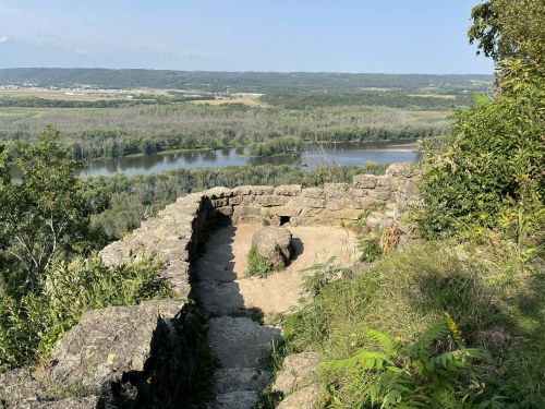 A scenic view from a rocky overlook, featuring a winding river and lush greenery in the background.