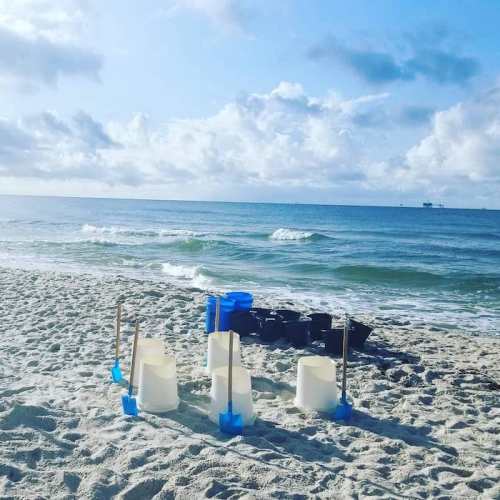 Beach scene with gentle waves, cloudy sky, and colorful sandcastle molds scattered on the sandy shore.