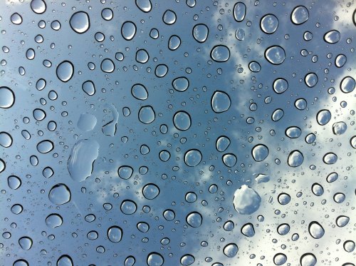 Close-up of water droplets on a glass surface, reflecting a cloudy blue sky.
