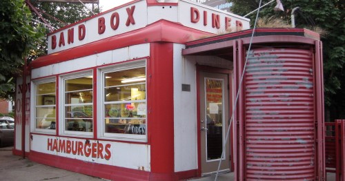 A red and white diner with "Band Box Diner" and "Hamburgers" signs, featuring large windows and a vintage design.
