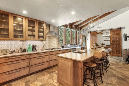 Modern kitchen with wooden cabinets, a large island, and stone flooring, featuring natural light and stylish decor.