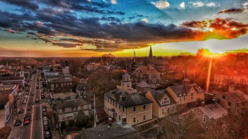 Aerial view of a small town at sunset, with colorful clouds and a church steeple silhouetted against the horizon.