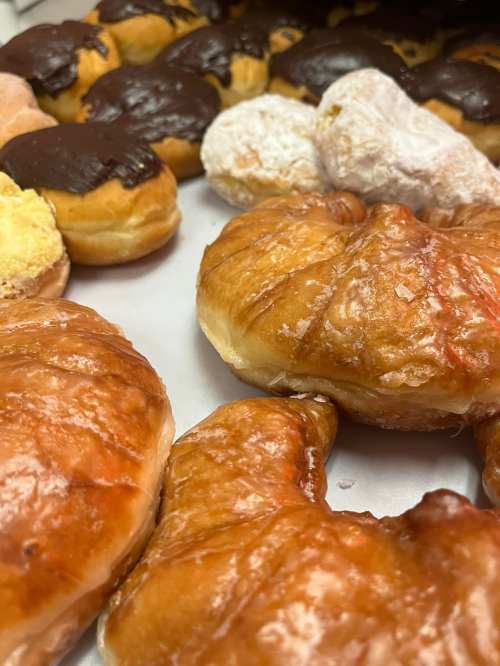 A close-up of assorted pastries, including glazed donuts and flaky croissants, arranged on a tray.