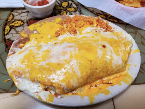A plate of cheesy enchiladas topped with melted cheese, served with rice and a side of salsa.