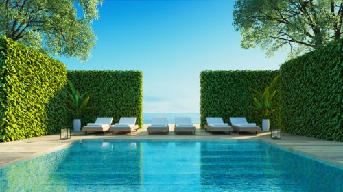 A serene pool area with lounge chairs, surrounded by lush greenery and a clear blue sky.