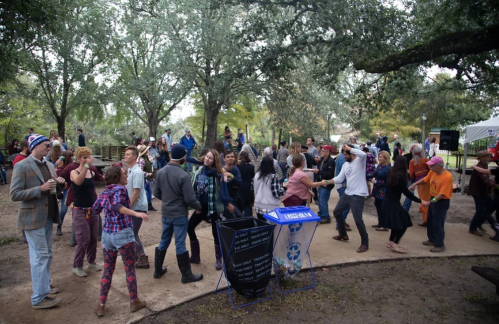 A lively outdoor gathering with people dancing and enjoying music under trees in a park.
