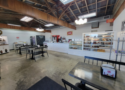 Bright bakery interior with wooden beams, display case of pastries, and tables for seating. Cozy and inviting atmosphere.