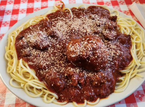 A plate of spaghetti topped with meatballs and marinara sauce, sprinkled with grated cheese, on a checkered tablecloth.