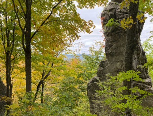 A rocky outcrop surrounded by vibrant autumn foliage and trees under a cloudy sky.