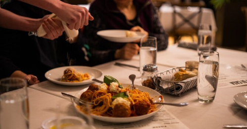 A table set with plates of spaghetti and meatballs, glasses of water, and diners enjoying a meal together.