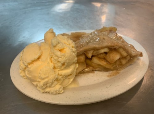A slice of apple pie with a scoop of vanilla ice cream on a white plate.