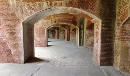 Interior of a brick building with arched doorways and a spacious, empty floor. Natural light illuminates the scene.