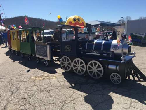 A colorful miniature train with a blue engine and yellow and green cars, decorated with festive flags, on a sunny day.