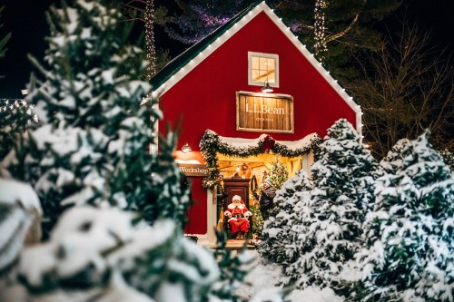 A cozy red workshop decorated for Christmas, with Santa sitting inside surrounded by snow-covered trees.