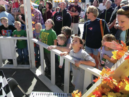 A group of children and adults watch an event with excitement, surrounded by a festive atmosphere.
