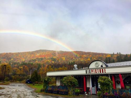 A colorful autumn landscape with a rainbow over a quaint building named "Big Picture" surrounded by trees.