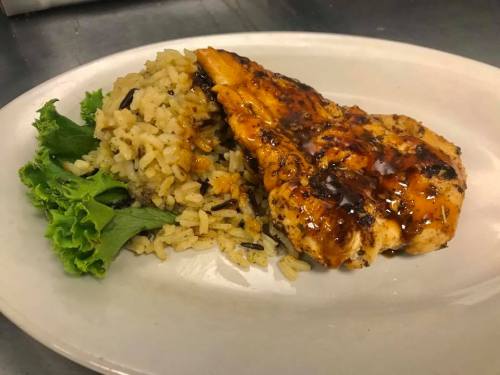 Grilled chicken breast with a glaze, served with seasoned rice and a side of fresh lettuce on a white plate.