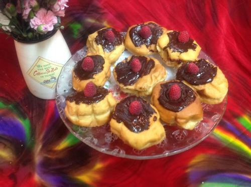 A plate of pastries topped with chocolate and raspberries, next to a vase of flowers on a colorful background.