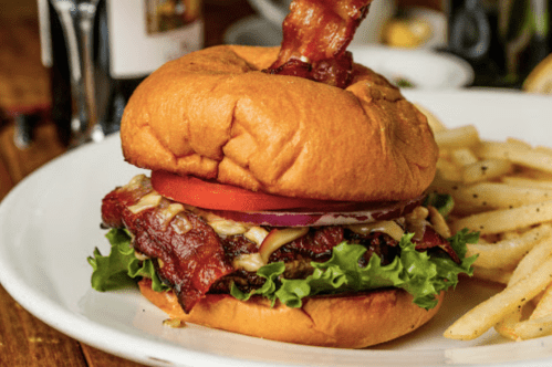 A juicy burger with bacon, lettuce, tomato, and onion on a toasted bun, served with a side of fries.
