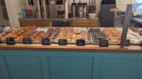 A display case filled with various donuts, labeled with flavors, in a bright, inviting bakery setting.