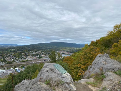 A scenic view from a rocky overlook, showcasing rolling hills and a cloudy sky above a small town below.