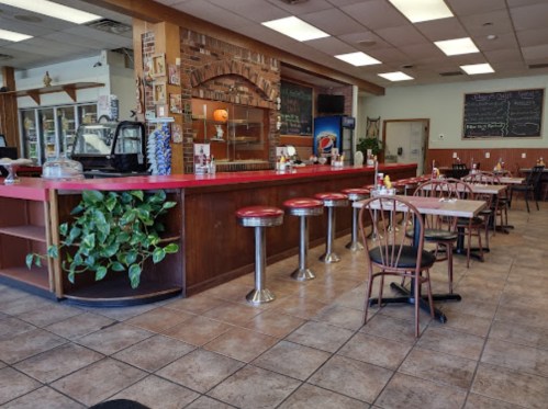 A cozy diner interior featuring a counter with stools, tables, and a menu board on the wall.