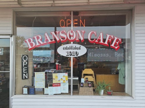 A storefront of Branson Cafe with an "Open" sign, featuring a welcoming display and established in 1910.