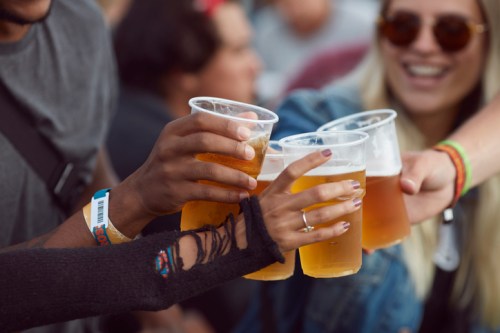 A group of friends toasting with plastic cups of beer at a lively outdoor event.