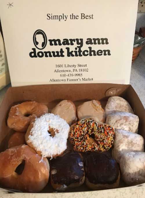 A box of assorted donuts from Mary Ann Donut Kitchen, featuring various toppings and flavors.