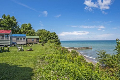 Cozy cabins by the shore, surrounded by greenery and a clear blue lake under a bright sky.