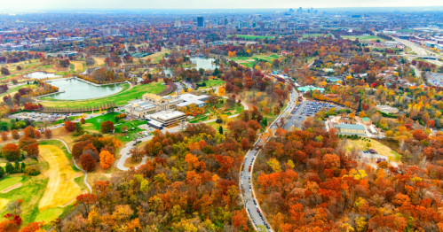 Aerial view of a vibrant autumn landscape with colorful trees, a golf course, and a city skyline in the distance.