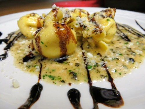 A plate of tortellini in a creamy sauce, garnished with herbs and drizzled with balsamic reduction.