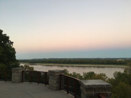 A serene river view at dusk, with soft pastel colors in the sky and lush greenery along the water's edge.