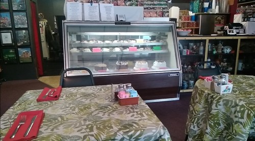 A cozy restaurant interior with tables set for dining and a display case filled with desserts in the background.