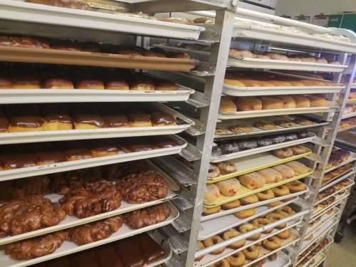 A bakery display with multiple trays of assorted donuts and pastries, showcasing a variety of flavors and toppings.
