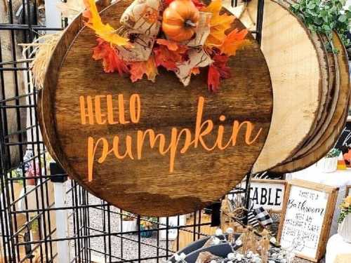 A wooden sign with "Hello Pumpkin" in orange, decorated with autumn leaves and a small pumpkin.