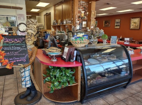 A cozy café interior featuring a display case, menu board, and a whimsical statue welcoming customers.