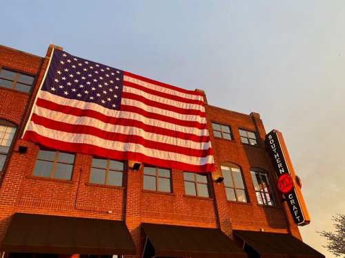 A large American flag hangs on a brick building with a sign for Southern Craft, illuminated by sunset light.