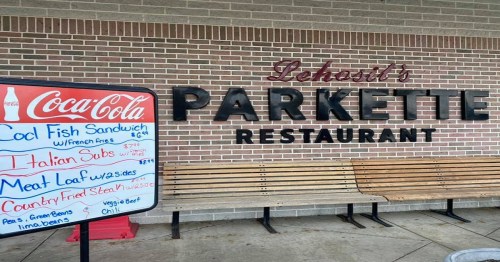 Sign for Lechats's Parkette Restaurant with a menu board featuring various dishes and prices. Benches are visible nearby.