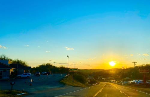 A sunset over a rural road, with cars parked along the side and a clear blue sky.