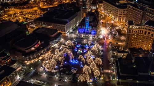 Aerial view of a city square adorned with festive lights and decorations, surrounded by buildings and parked cars at night.