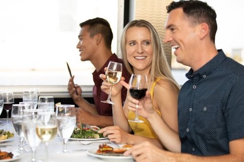 A group of friends enjoying a meal together, toasting with drinks and smiling at each other at a dining table.