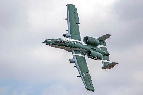 A military aircraft performing a steep bank maneuver against a cloudy sky.