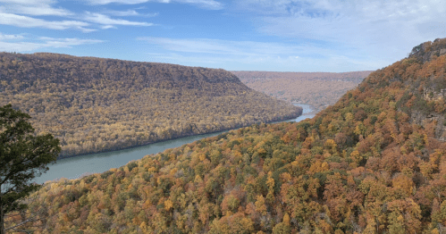 A scenic view of a river winding through a valley surrounded by autumn-colored trees and rolling hills.