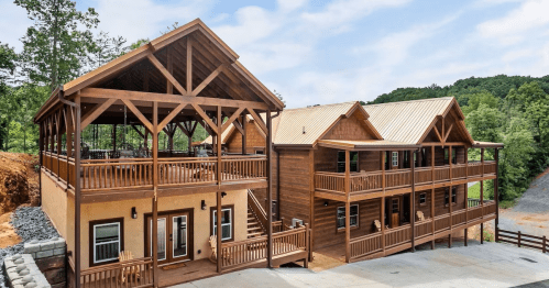 A large wooden cabin with multiple levels, featuring balconies and a spacious outdoor deck surrounded by trees.
