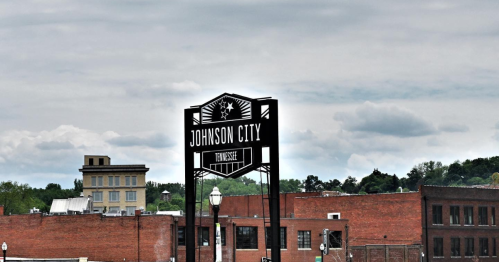 Sign for Johnson City, Tennessee, against a cloudy sky, with brick buildings in the foreground.