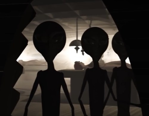 Three tall, slender alien figures with large heads and dark eyes stand in a dimly lit room, partially obscured by shadows.