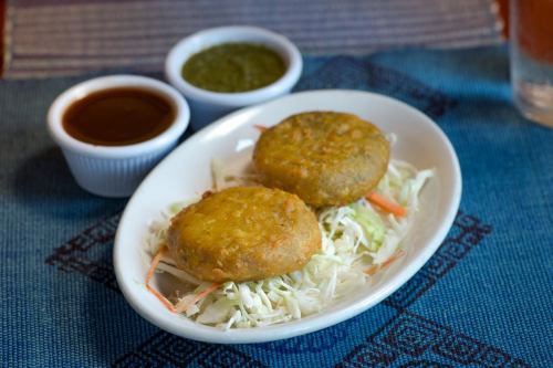 Two golden-brown patties on a bed of shredded cabbage, accompanied by green and brown sauces in small bowls.