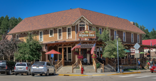 The Alpine Inn Restaurant, a multi-story brown wooden building with a large patio, on a sunny day.