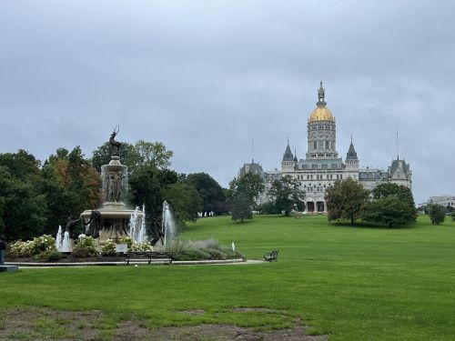 A fountain in a park with a grand building featuring a golden dome in the background under a cloudy sky.